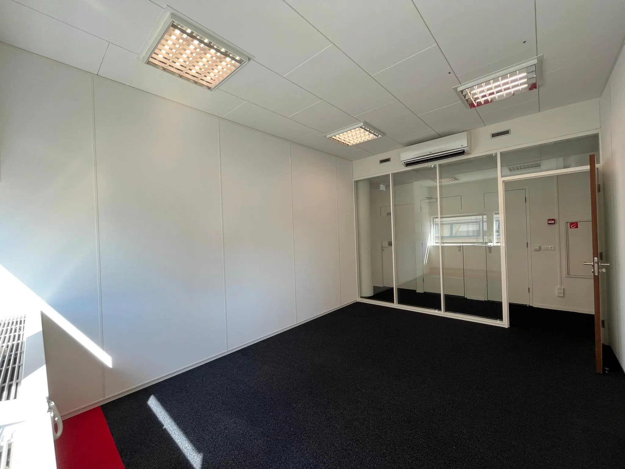 Leeg kantoor in Leidse Rijn met glazen wand, zwarte vloerbedekking en ingebouwde plafondverlichting.